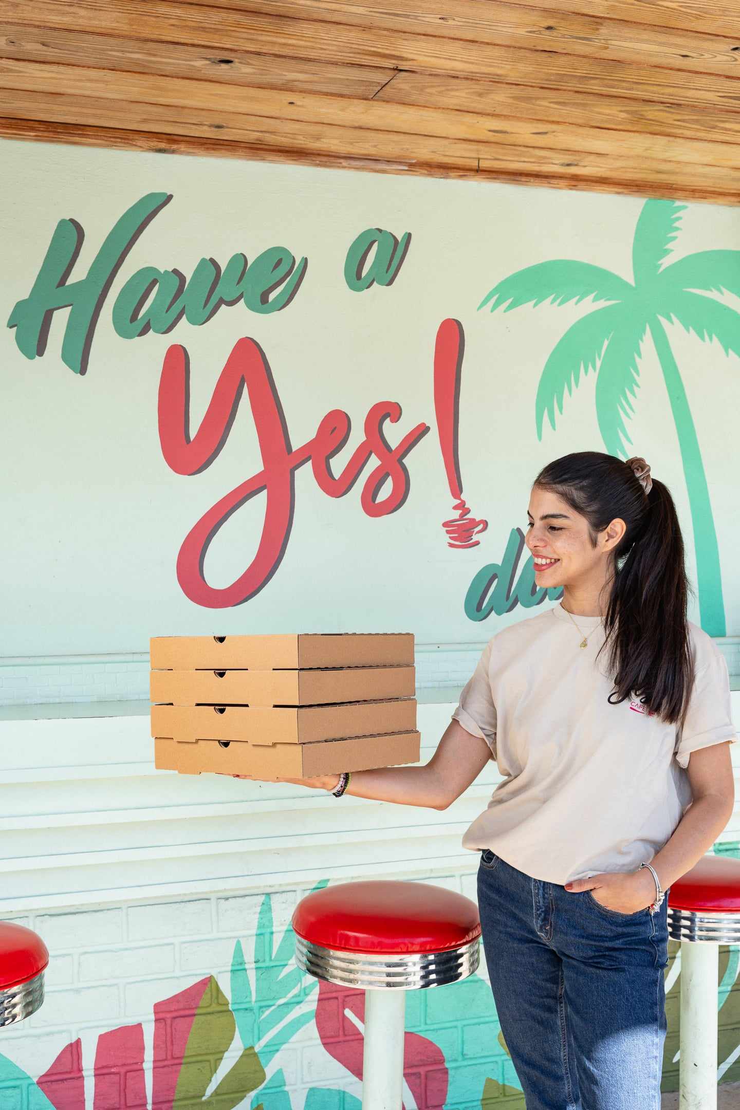 A stack of pizza boxes carried in front of the Have a Yes! day mural