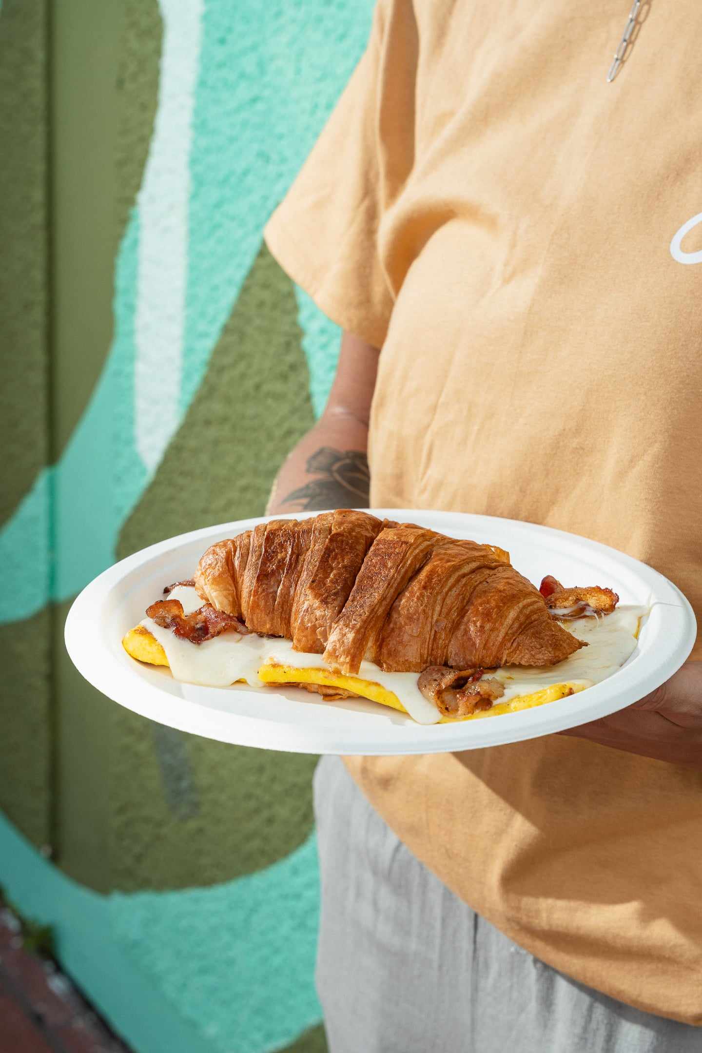 A croissant sandwich with egg and bacon on a paper plate