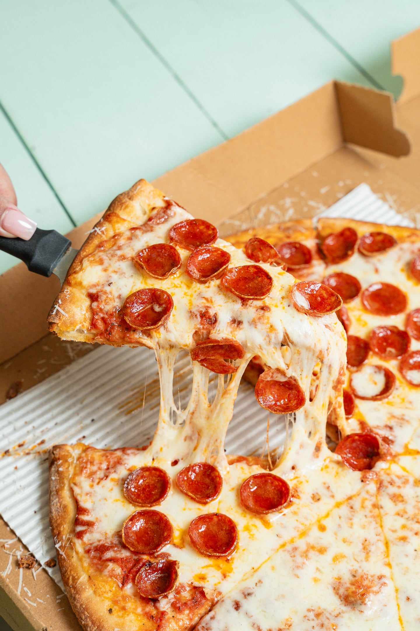 A slice of pepperoni pizza lifted from the pie with the cheese stretching