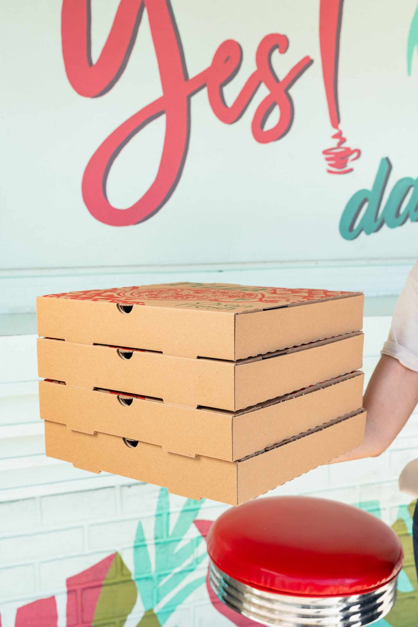 A stack of pizza boxes on the counter in front of the Have a Yes! day mural