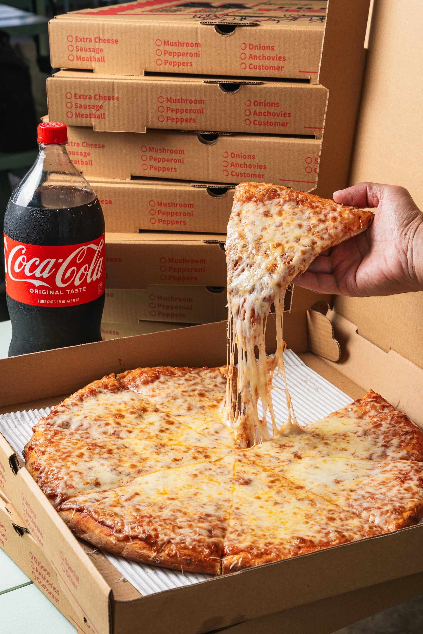 A slice of cheese pizza lifted from the pie with the cheese stretching, next to a bottle of Coca-Cola