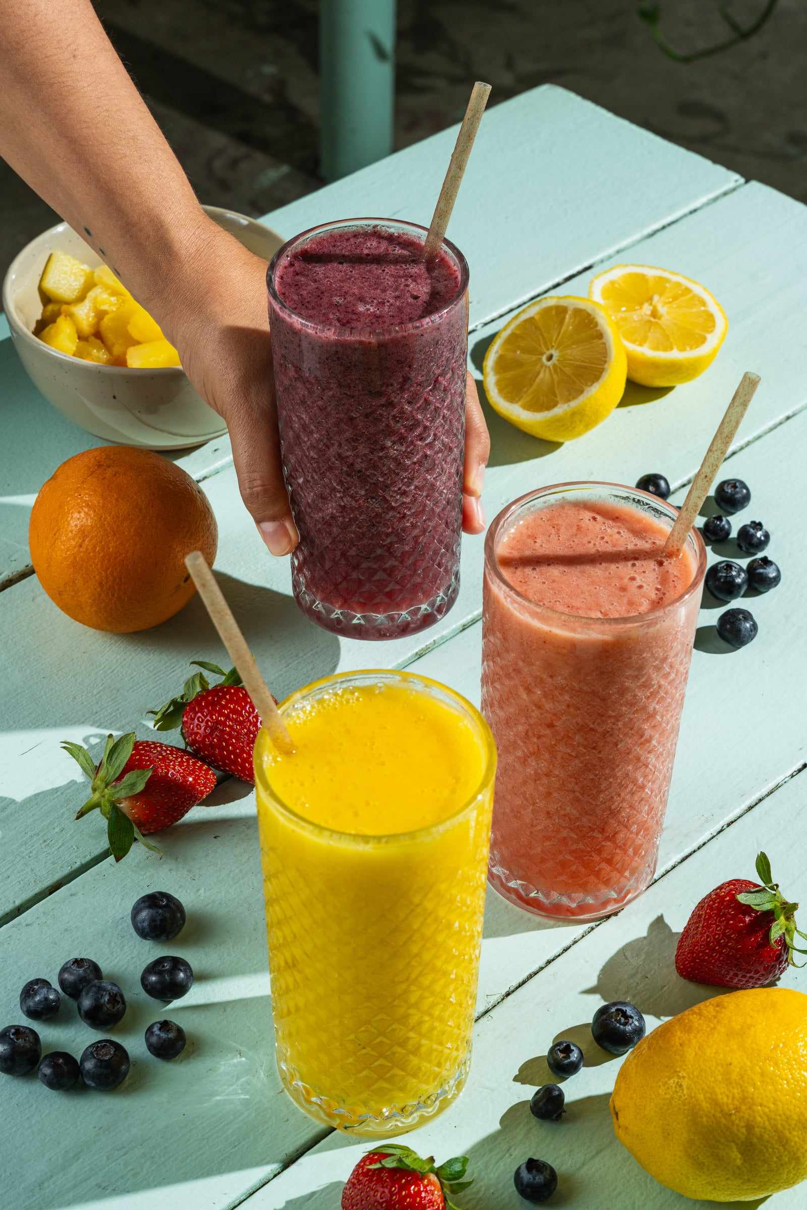 Berry, mango and strawberry smoothies with fresh fruit around them