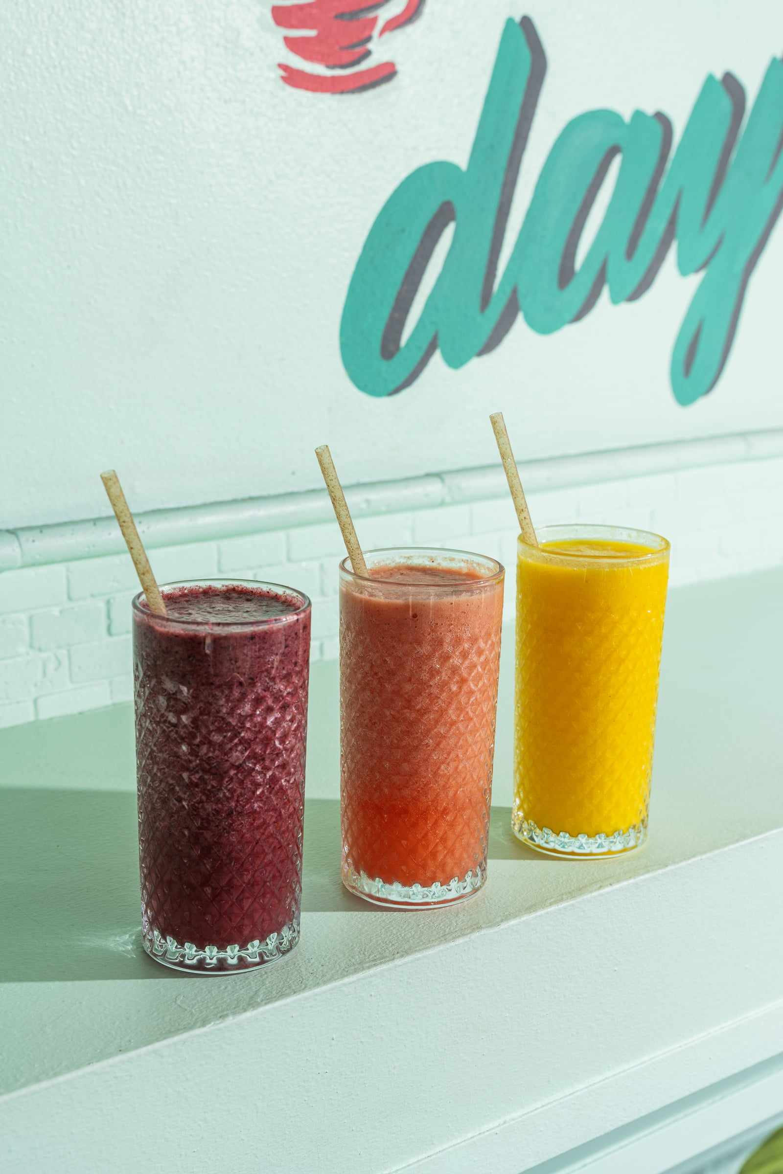 Three fruit smoothies in tall glasses in front of the Yes! mural