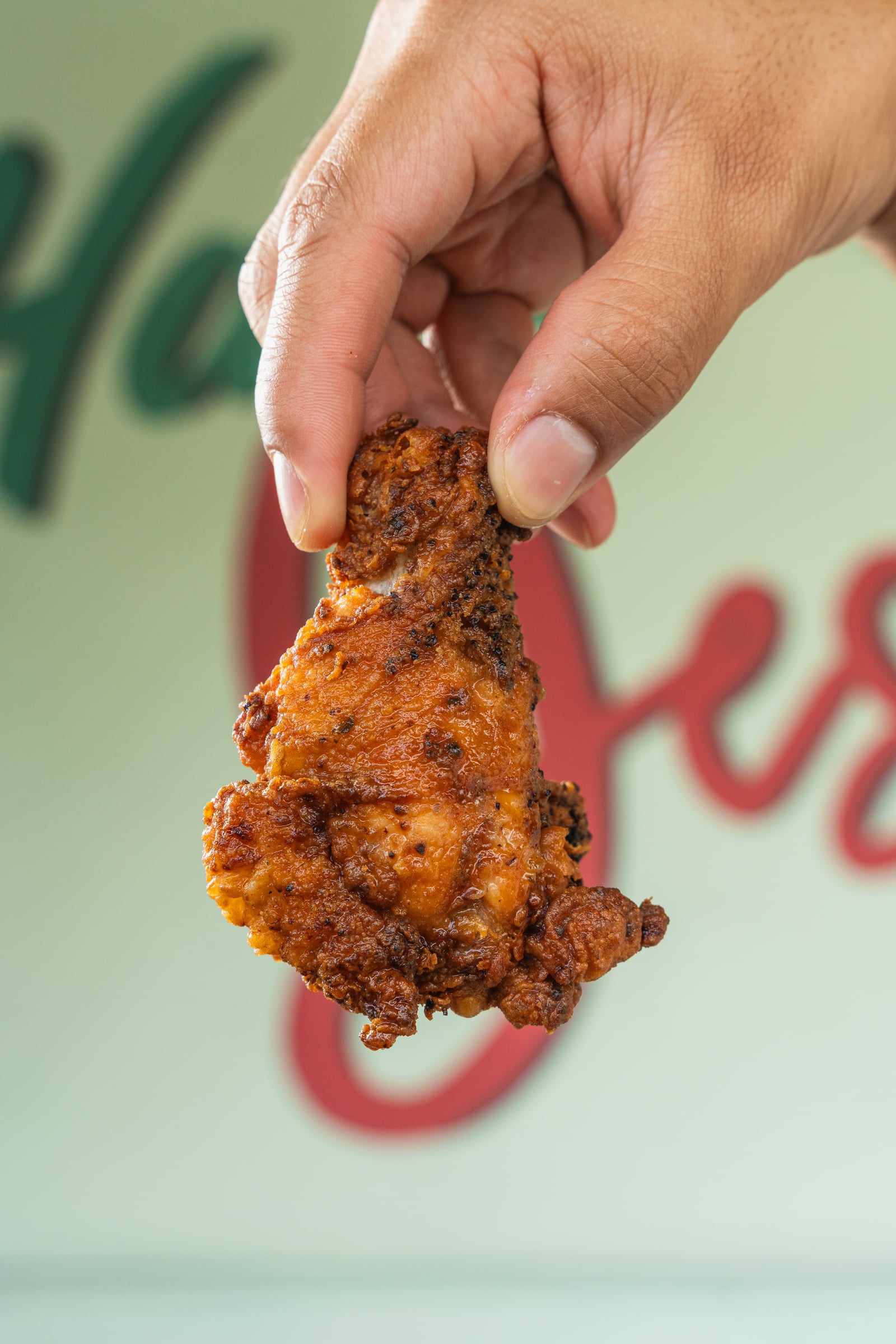 A crispy jumbo wing held up in front of the Yes! mural