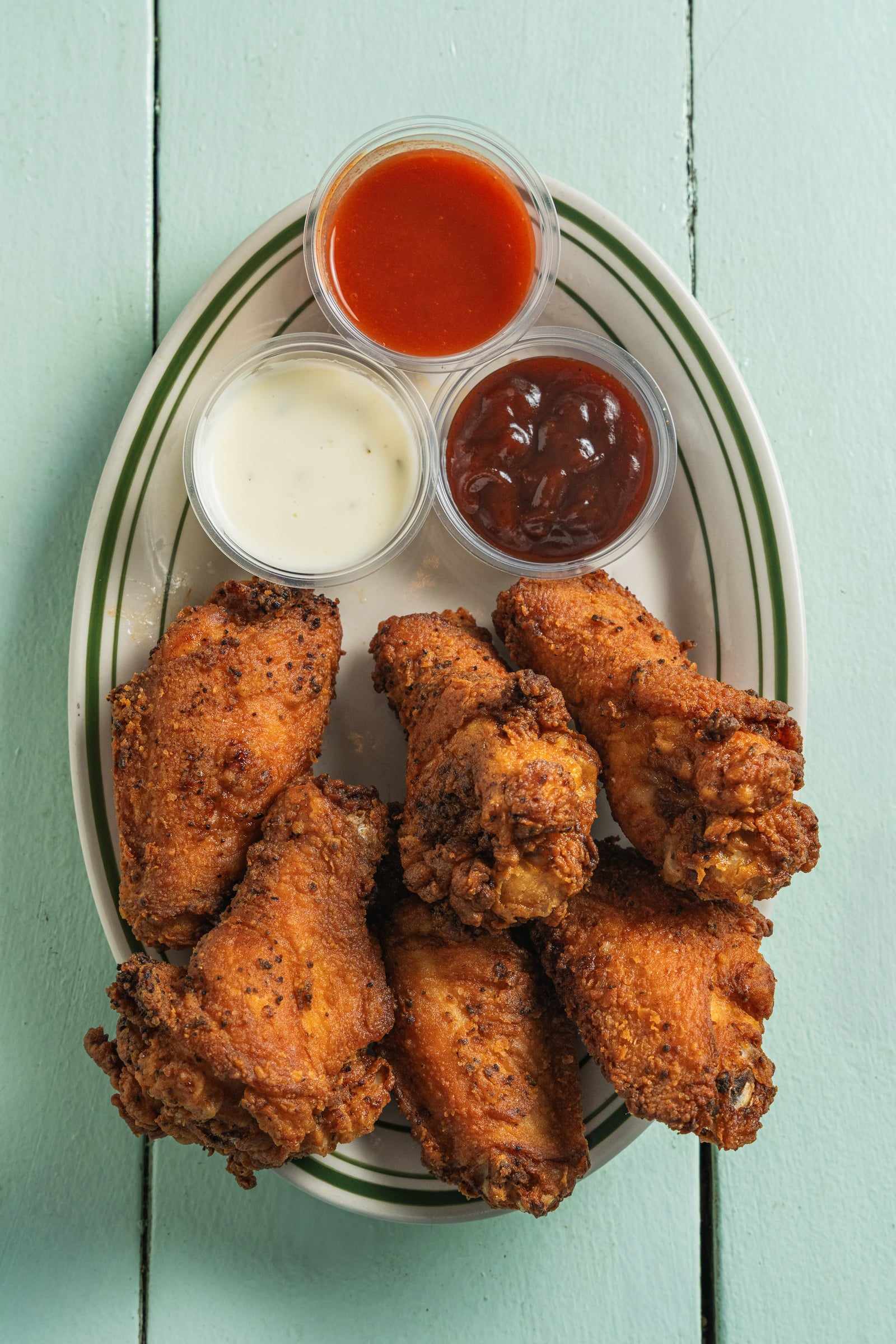 Crispy jumbo wings on a plate with ranch and hot sauce cups