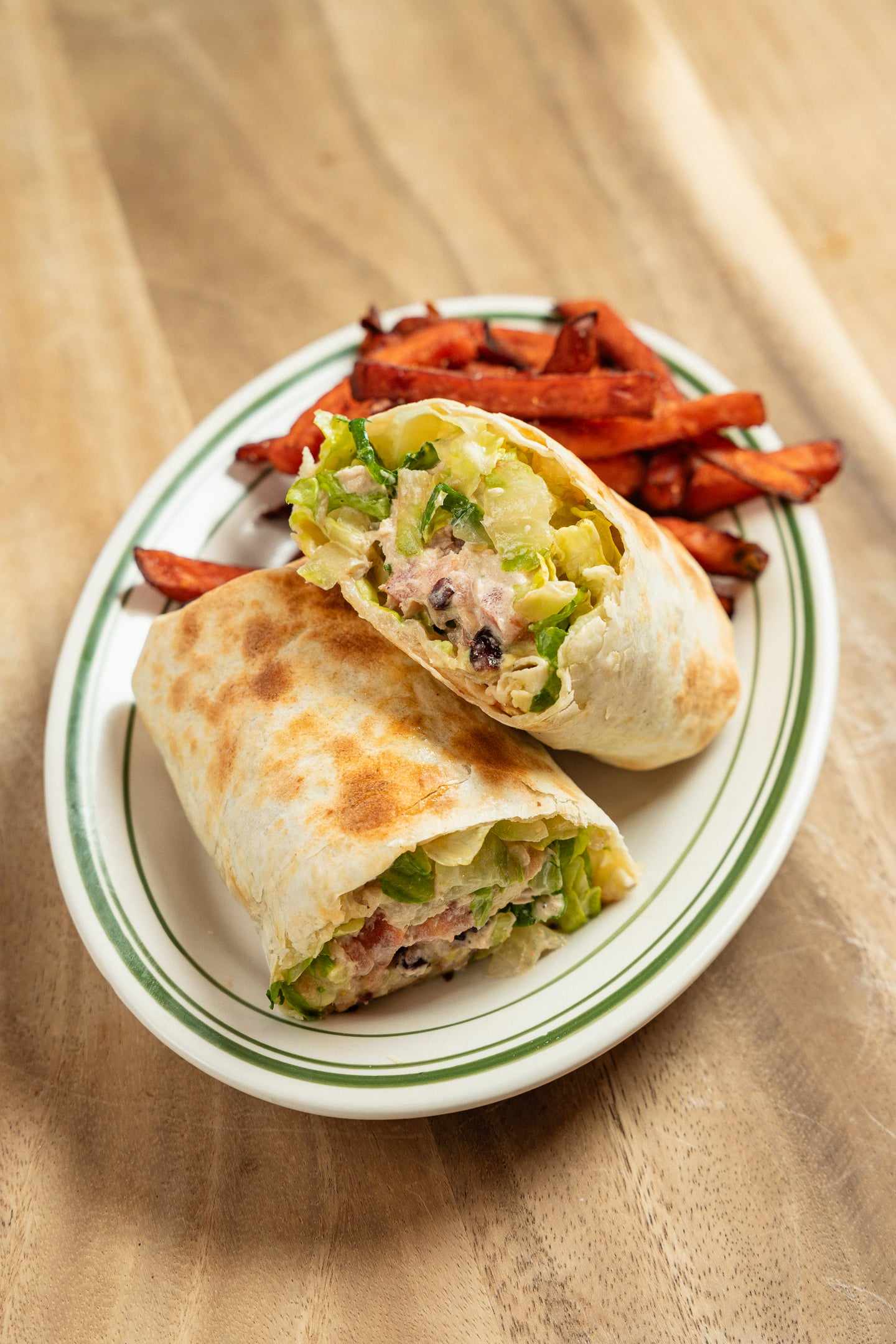A grilled wrap cut in half on a plate with sweet potato fries