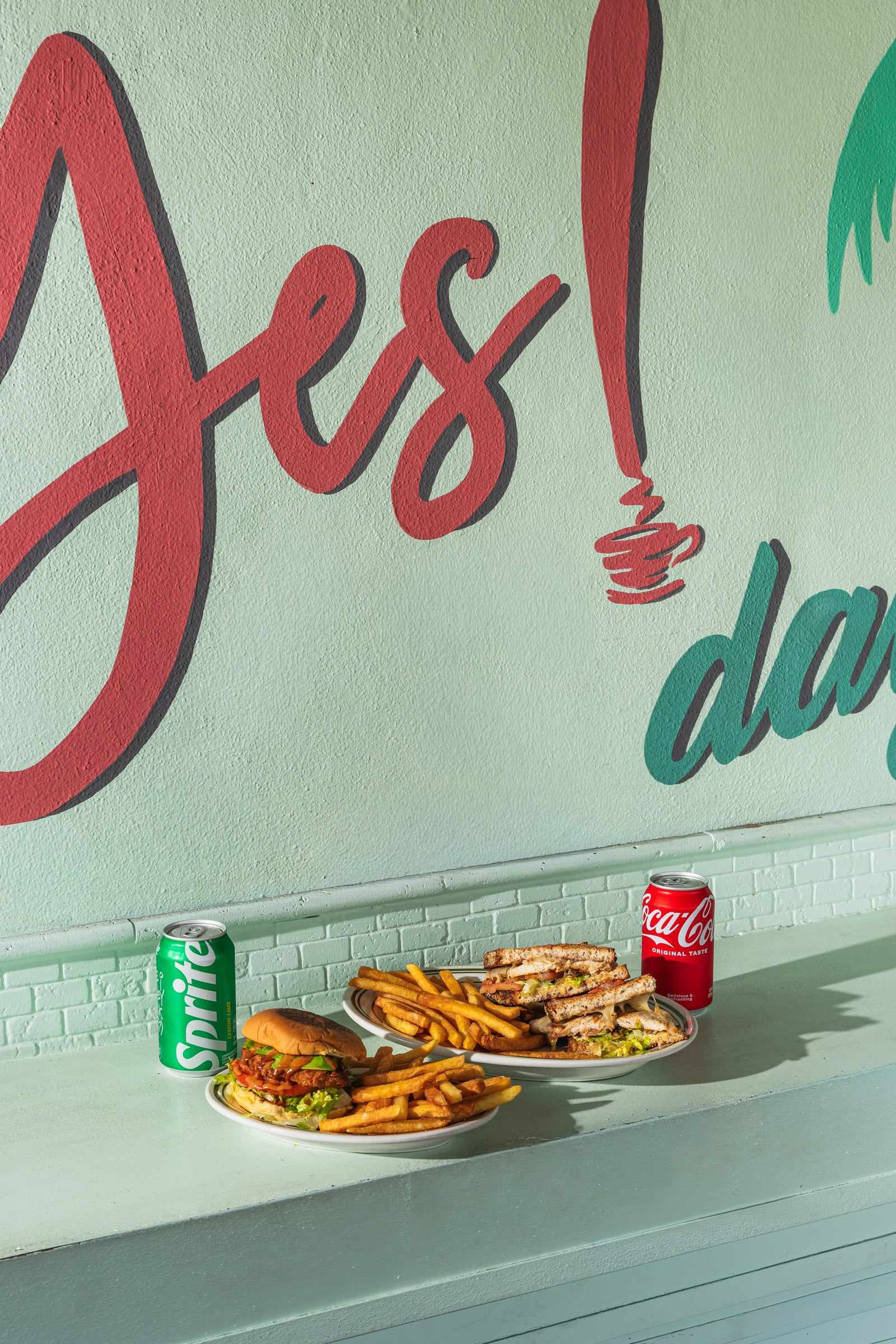 A burger with fries and a can of Sprite in front of the Yes! day mural